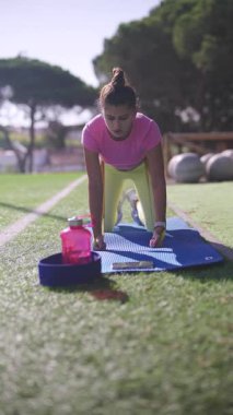 Genç bir kadın, sıcak güneş ışığında, elinde su şişesiyle dışarıda spor yapıyor.