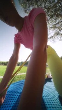 Bir insan yemyeşil ve parlak güneş ışığıyla çevrili bir minder üzerinde açık havada esneme egzersizleri yapıyor.