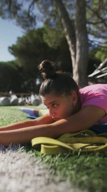 Odaklanan ve kendini yogaya adamış bir birey, bir paspas üzerinde esneme bandı kullanırken açık havada yoga yapıyor.