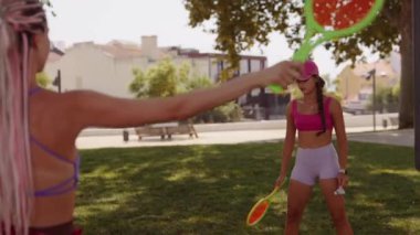 Bugün güneşli, canlı bir park ortamında iki kadın birlikte neşeli bir tenis oyununun keyfini çıkarıyorlar.