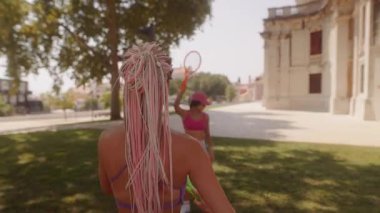 Güneşli bir parkta renkli raketlerle oynayan iki canlı kadın heyecan verici, aktif bir açık hava gününün tadını çıkarıyorlar.