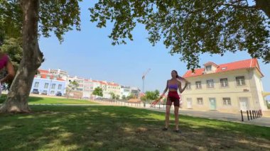 Güneşli bir parktaki açık hava oyununa neşeyle katılan iki kadın hem spor hem de arkadaşlığı destekliyor.