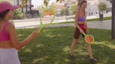 Güneşli bir günde, iki arkadaş bereketli yeşilliklerle dolu canlı bir şehir parkında raket oynamayı severler.