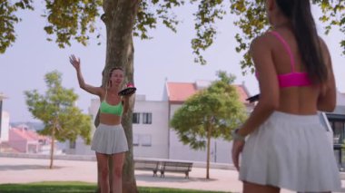 Güneşli bir parkta canlı ve canlı bir raket oyununun keyfini çıkaran iki kadın.