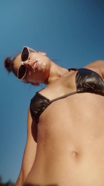 Şık bir kadın, plajda şık bir bikini ve son moda güneş gözlüğü giyerken sıcak güneşin tadını çıkarıyor.