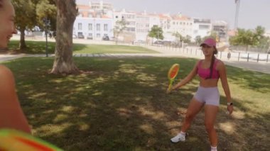 Aydınlık ve güneşli bir günde, iki arkadaş güzel bir parkta renkli raketlerle oynarken eğleniyor.