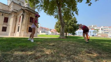 İki arkadaş güneşli bir parkta raketler ve bol miktarda enerjiyle sporun tadını çıkarıyorlar.