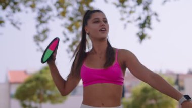 Neşeli genç bir kadın, canlı pembe spor bir bluz giyiyor, açık havada eğlenmekten zevk alıyor, elinde kürek çekiyor.