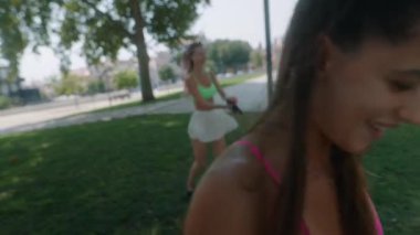 İki hevesli kadın, güneşli bir parkta renkli kıyafetleriyle enerjik bir çalışma yapıyorlar.