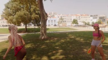 Parkta güneşli bir günde renkli raketler kullanırken iki enerjik kadın dışarıda eğleniyor.