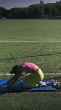 Odaklanmış bir birey, bir spor sahasındaki direniş bandının yardımıyla dinamik esneme hareketleri gerçekleştiriyor.