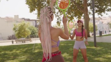 İki kadın, güneşli bir parkta güneşli bir günde, enerjik bir tenis maçına çıkıp eğleniyorlar.