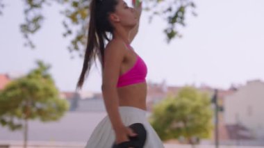 Pembe ekin bluzlu genç bir kadın doğada renkli ekipmanlarla canlı bir antrenmanın tadını çıkarıyor.