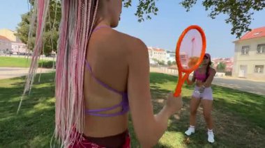 İki arkadaş mutlu bir şekilde parkta güneşli, güneşli bir günün tadını çıkarıyor raketlerle oynuyor ve dışarıda eğleniyorlar.