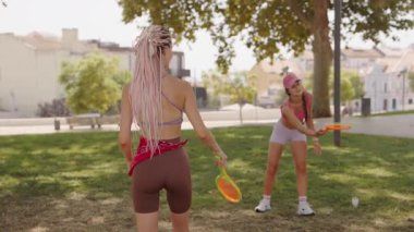 Güneşli bir günde, iki arkadaş neşeli bir şekilde parkta disk oyunları oynuyorlar, sağlık ve keyfi destekliyorlar.