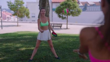 İki arkadaş parkta frizbi oynayarak, canlı giysiler ve aktif yaşam tarzını sergileyerek güneşli bir günün tadını çıkarıyorlar..