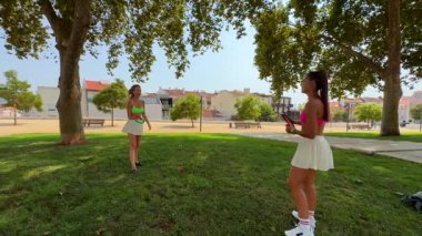 Yeşilliklerle dolu canlı bir parkta iki kız güneşin altında eğlenceli bir oyun oynuyor.