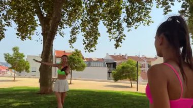 Parkta güneşli bir günün tadını çıkaran iki arkadaş, canlı kıyafetler giyiyorlar ve neşe dolu kahkahalar atıyorlar.