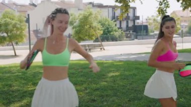 Arkadaşlar parlak giysiler içinde eğlenirler, neşe dolu güneşli bir parkta açık hava oyunları oynarlar.