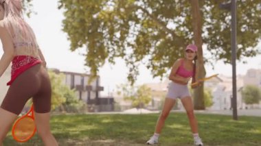 Parlak ve güneşli bir parkta, iki hevesli arkadaş birlikte canlı tenis antrenmanı yapıyorlar.