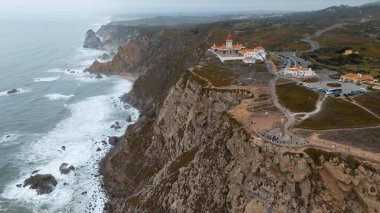 Nefes kesici uçurumları, deniz fenerini ve manzaralı bir sahil şeridi boyunca dalgaları yakalayan çarpıcı hava manzarası.