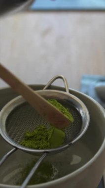 Bir bambu kepçesi ve süzgeci kullanarak mükemmel bir demleme yapmak için matcha çayı hazırlama görüntüsü.