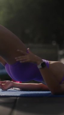 Bir kadın yoga minderinde çekirdek egzersizi yaparken açık hava manzarasının keyfini çıkarıyor.