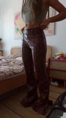 Şık bir model, rahat bir yatak odasında, modaya uygun pantolonlar ve şık bir hasat bluzu içinde rahatça poz verir.