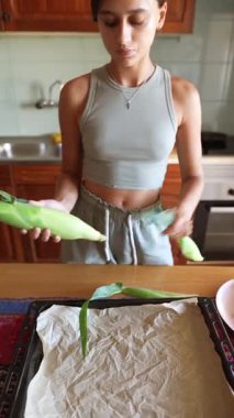 Bir insan parlak bir mutfakta taze mısır hazırlıyor, canlı renkler ve yemek pişirme aktiviteleri sergiliyor..