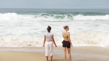 İki yakın arkadaş okyanusun kıyısında güzel ve neşeli bir anı paylaşıyor. Çarpışan dalgaları mutlu bir şekilde işaret ediyorlar.