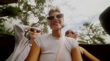 Arkadaşların neşeli bir sahnesi. Üstü açık bir arabanın keyfini çıkarıyorlar. Güneş gözlüğü takıyorlar ve keyifle gülümsüyorlar.