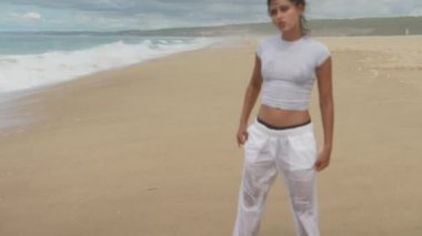 Genç bir kadın güzel sahilde rahatça geziniyor, ayaklarına gelen hafif dalgaların tadını çıkarıyor.