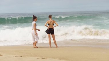 İki kadın sahilde harika vakit geçiriyorlar, neşeyle dalgaların ve güzel manzaranın tadını çıkarıyorlar.
