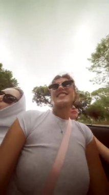 Bir grup arkadaş bulutlu gökyüzünün altında üstü açık şık bir arabada kaygısız bir şekilde eğleniyorlar.