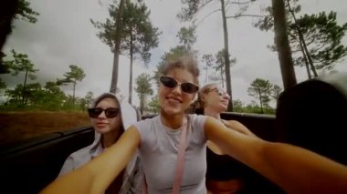 Üç neşeli kız, yukarıdaki canlı gökyüzünün tadını çıkarırken şık, üstü açık bir arabada keyifli bir yolculuk yapıyorlar.