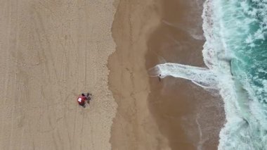 Güneşli bir sahilde huzur içinde uzanan güzel bir çifti bir hava görüntüsü çeker. Hafif dalgalar kıyıya vururken.