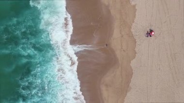 Sersemletici turkuaz dalgaların kumlu bir sahile enerji dolu bir şekilde çarpışının nefes kesici hava manzarasını deneyimleyin.