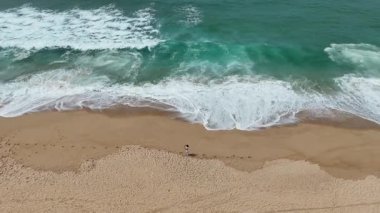 Yumuşak, nazik dalgaların olduğu sakin bir sahil sahnesi ve derin güzelliklerden keyif alan yalnız bir figür.