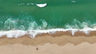 Bir hava çekimi sahile çarpan çarpıcı dalgaları yakalar, altın kumdaki hassas ayak izlerini ortaya çıkarır.