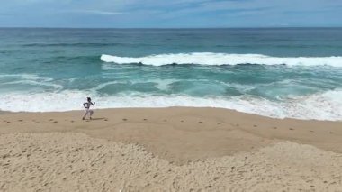Neşeli bir çocuk güneşli sahil boyunca koşar, çarpan dalgaların ve barışçıl okyanus çevresinin tadını çıkarır.