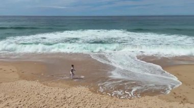 Güzel, huzurlu bir sahne. Resimli kumlu bir sahil boyunca neşeyle koşan biri. Yakınlarda dalgalar çarpıyor.