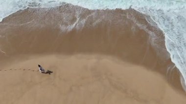 Sahilde tek başına yürüyen bir insanın barışçıl bir görüntüsü. Dalgalar kumlarda desenler oluşturur.