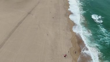 Yumuşak kum, turkuaz dalgalar ve neşeli plaja gidenlerin yer aldığı nefes kesici bir kumsal manzarası.