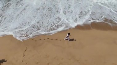 Hava görüntüsü, sahil boyunca sakin bir şekilde yürüyen ve yumuşak kumda ayak izleri bırakan birini gösteriyor.