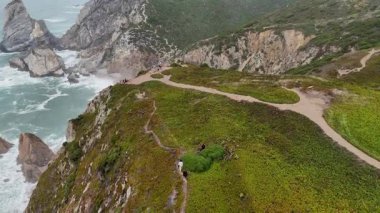 Güzel bir hava manzarası altında dalgalar olan kayalıklar boyunca zarifçe kıvrılan bereketli bir kıyı yolu gösteriyor.