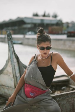 Tarz sahibi bir şahıs, şık moda anlayışını sergileyerek, liman kenarında zarif bir poz verir.