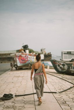 Bir kadın, çeşitli tekneler ve huzurlu bir sahil atmosferi ile çevrili güzel liman boyunca rahatça dolaşır.