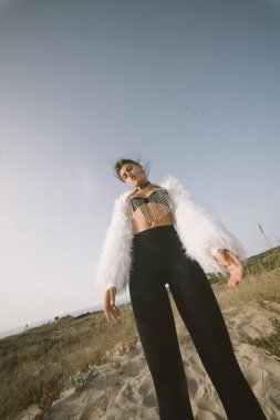 Moda kıyafetli şık bir manken kumsalda güven içinde poz verir, modayla doğal güzelliği harmanlar.