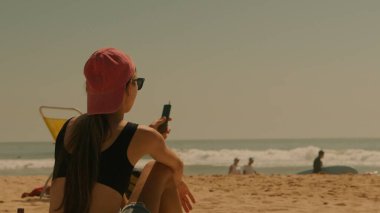 Huzurlu ve huzurlu bir an, güzel bir sahilde, bir akıllı telefon kullanarak boş zamanı ve modern hayatı yakalıyor.