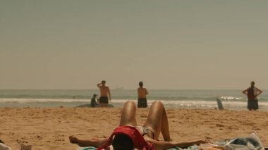 Güneşlenenlerin, sörfçülerin ve son derece sakin okyanus sularının sergilendiği sakin ve sakin bir sahil sahnesi.